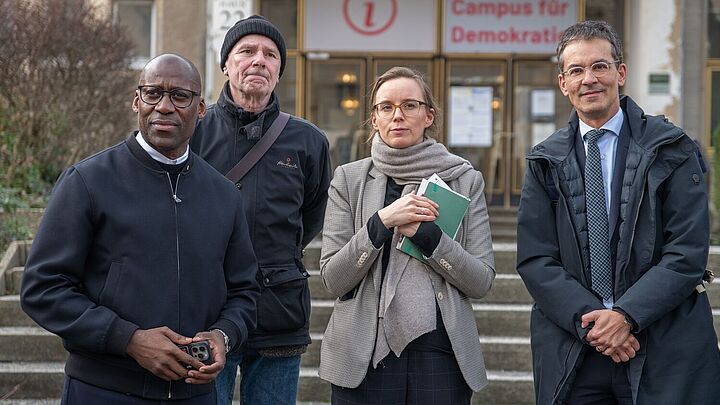 Joe Chialo, Olaf Weißbach, Lena Kuhl und Robin Mishra stehen nebeneinander vor 'Haus 22' auf dem Campus für Demokratie.