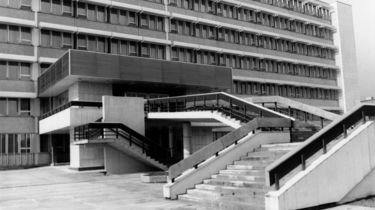 Das Schwarz-Weiß-Bild zeigt einen Teil des Stasi-Krankenhauses in Berlin-Buch. Zu sehen ist der Haupteingang mit einem kleinen Anbau, zu welchem eine Treppe hinaufführt.